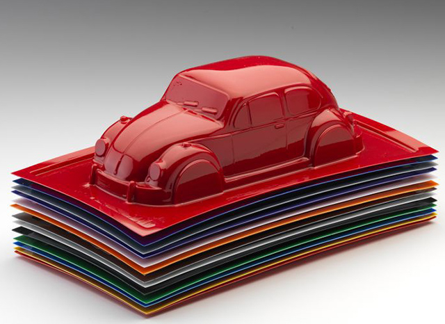 Một m&ocirc; h&igrave;nh &ocirc; t&ocirc; cổ điển m&agrave;u đỏ b&oacute;ng, giống như một chiếc Volkswagen Beetle, được đặt tr&ecirc;n một chồng c&aacute;c tấm nhựa h&igrave;nh chữ nhật, nhiều m&agrave;u sắc, gọn g&agrave;ng. Chiếc xe v&agrave; c&aacute;c tấm trải c&oacute; bề mặt s&aacute;ng b&oacute;ng, phản chiếu, thể hiện C&ocirc;ng nghệ tạo h&igrave;nh ch&acirc;n kh&ocirc;ng bằng nhựa t&ugrave;y chỉnh với chất lượng đẳng cấp thế giới tr&ecirc;n nền chuyển m&agrave;u đơn giản từ trắng sang x&aacute;m